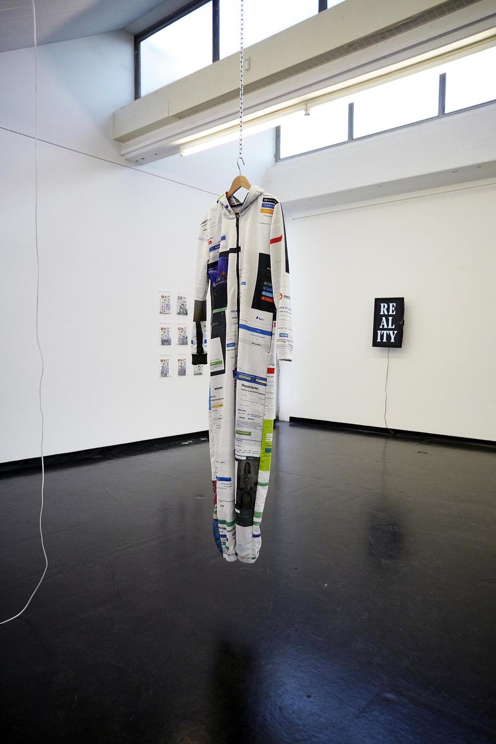 HIGH RES LOW BROW — a onesie printed with log-in screens, hanging in the space