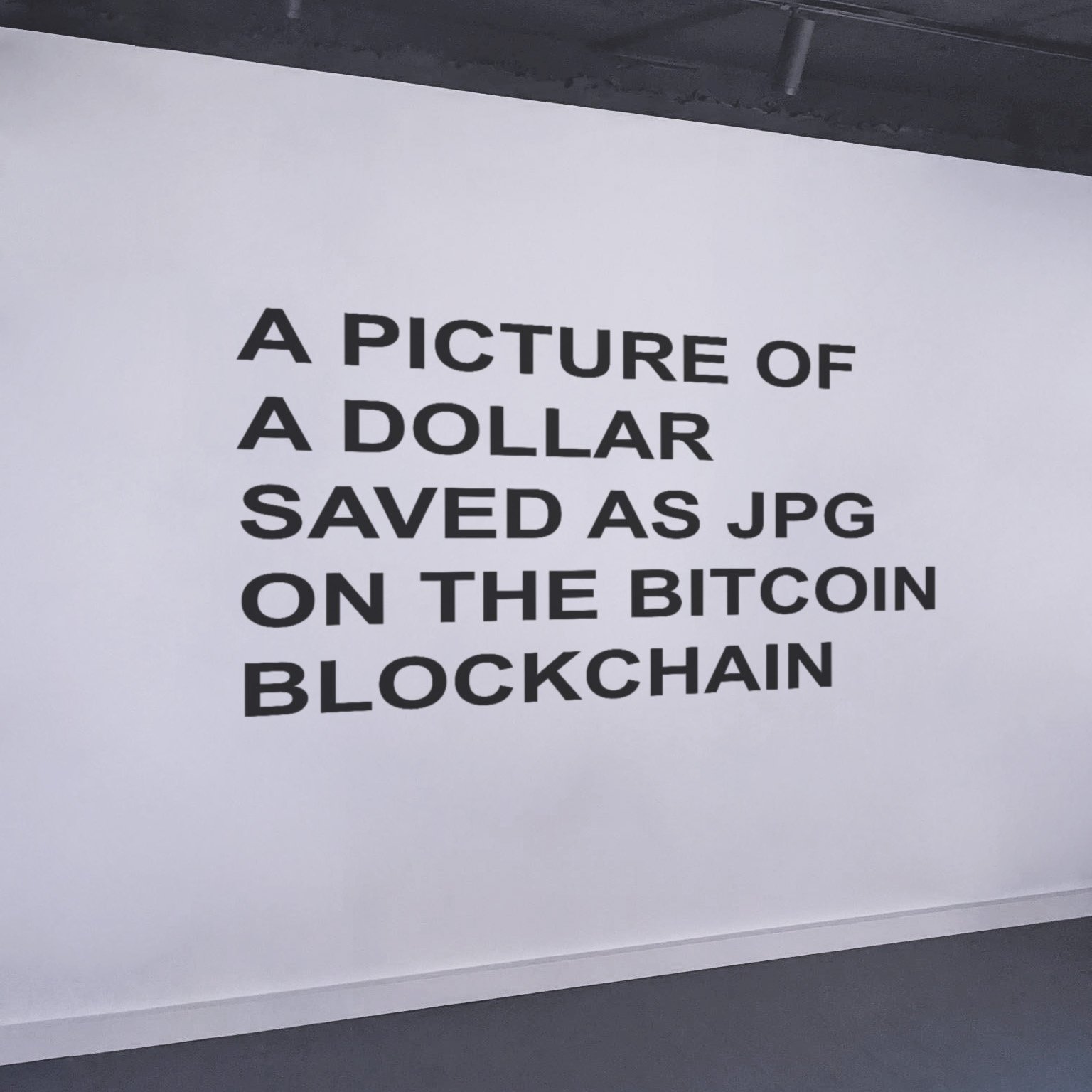 The work itself: the sentence A PICTURE OF A DOLLAR SAVED AS JPG ON THE BITCOIN BLOCKCHAIN in Arial Bold